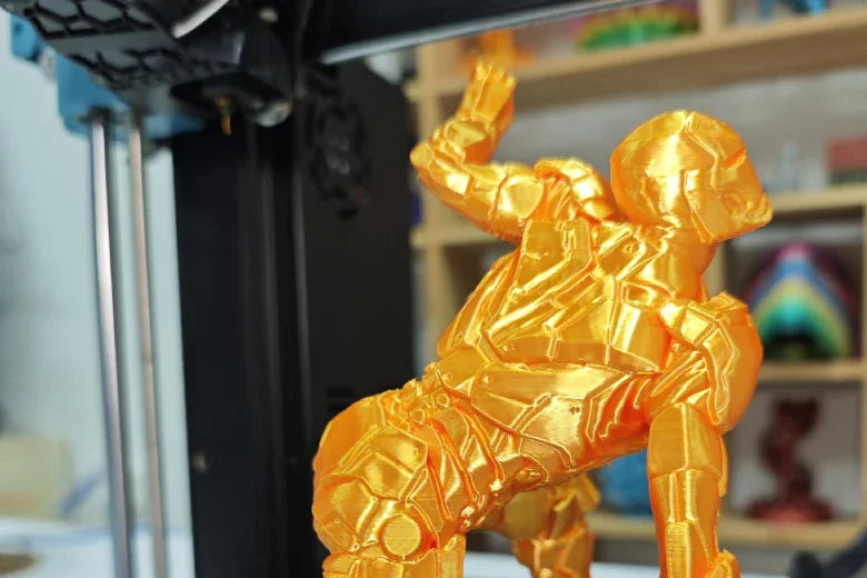 Golden 3D printed robot figure on a desktop 3D printer in a workshop setting