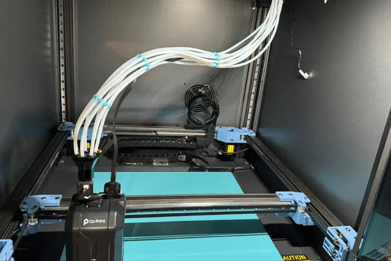 Large 3D printer with multiple filament tubes and a Co Print setup inside an enclosure.