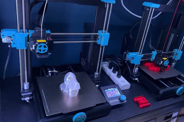 Two Sovol 3D printers printing plastic models on a desktop workspace