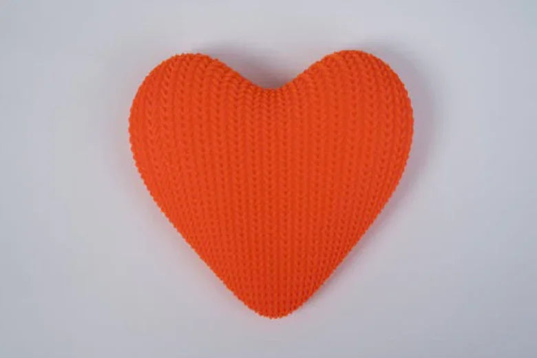 Orange knitted heart-shaped pillow on a plain white background