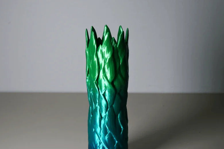 Green and blue gradient sculpted vase with pointed top on a plain surface