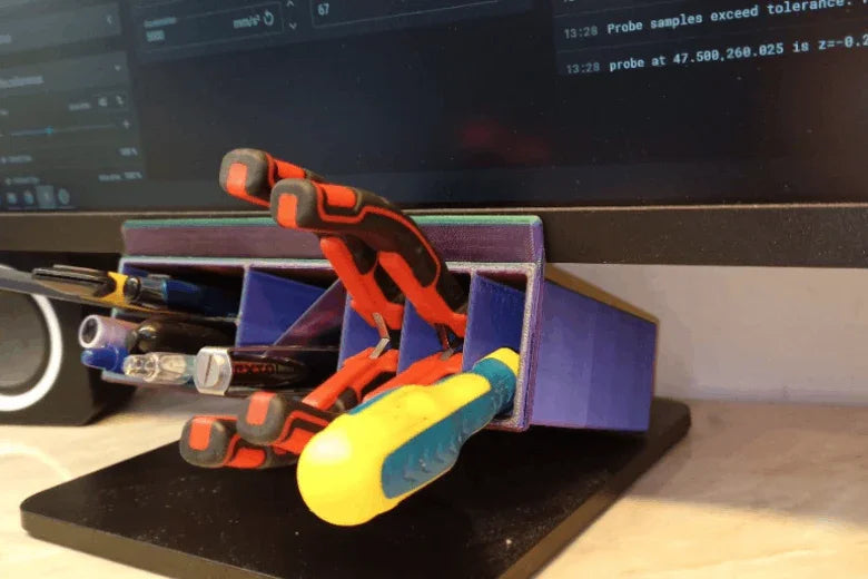 3D printed desk organizer holding pens, screwdriver, and clamps under computer monitor