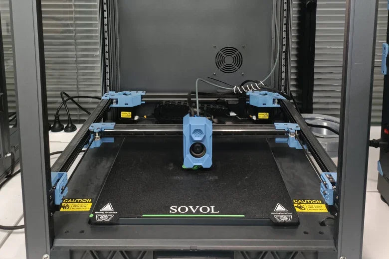 Sovol 3D printer in operation with blue extruder and safety labels in a workshop setting