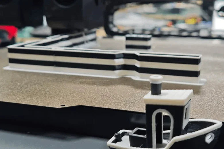 Dual-color 3D printer creating striped model objects on textured print bed