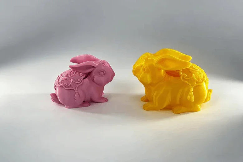 Pink and yellow 3D printed bunny figurines with decorative details on a white background