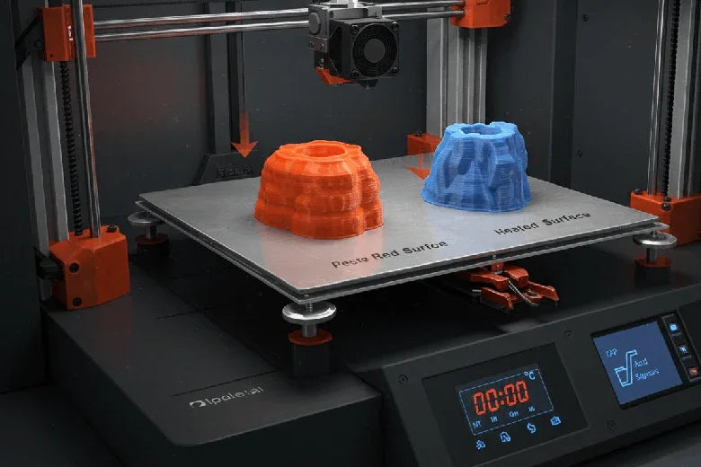 3D printer with heated bed showing red and blue plastic prints on labeled surfaces