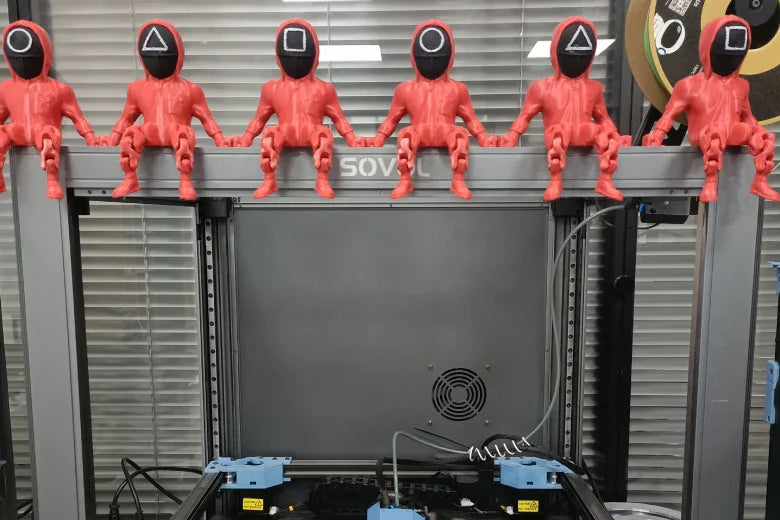 3D printed Squid Game guard figurines in red sitting on a Sovol 3D printer