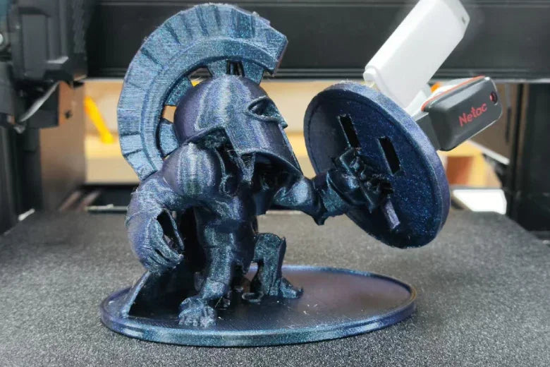 3D printed Spartan warrior figure holding shield on printer bed, USB device in background